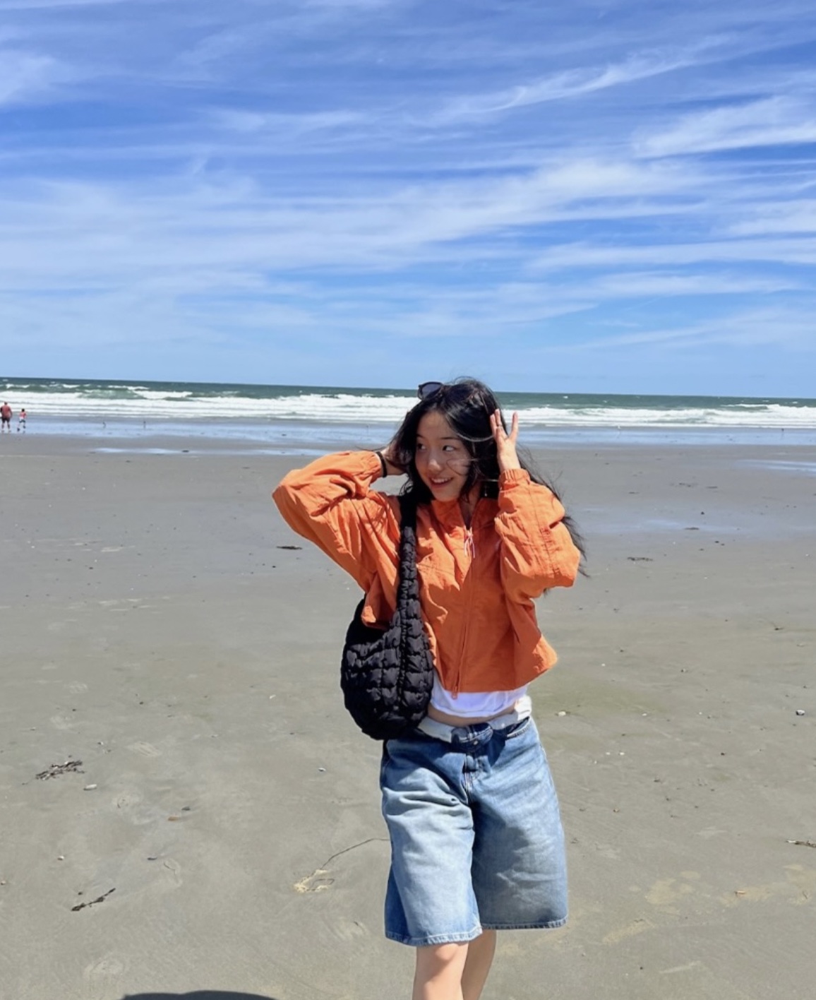 Lucy Park in an orange jacket on a windy beach, smiling and looking over her shoulder.